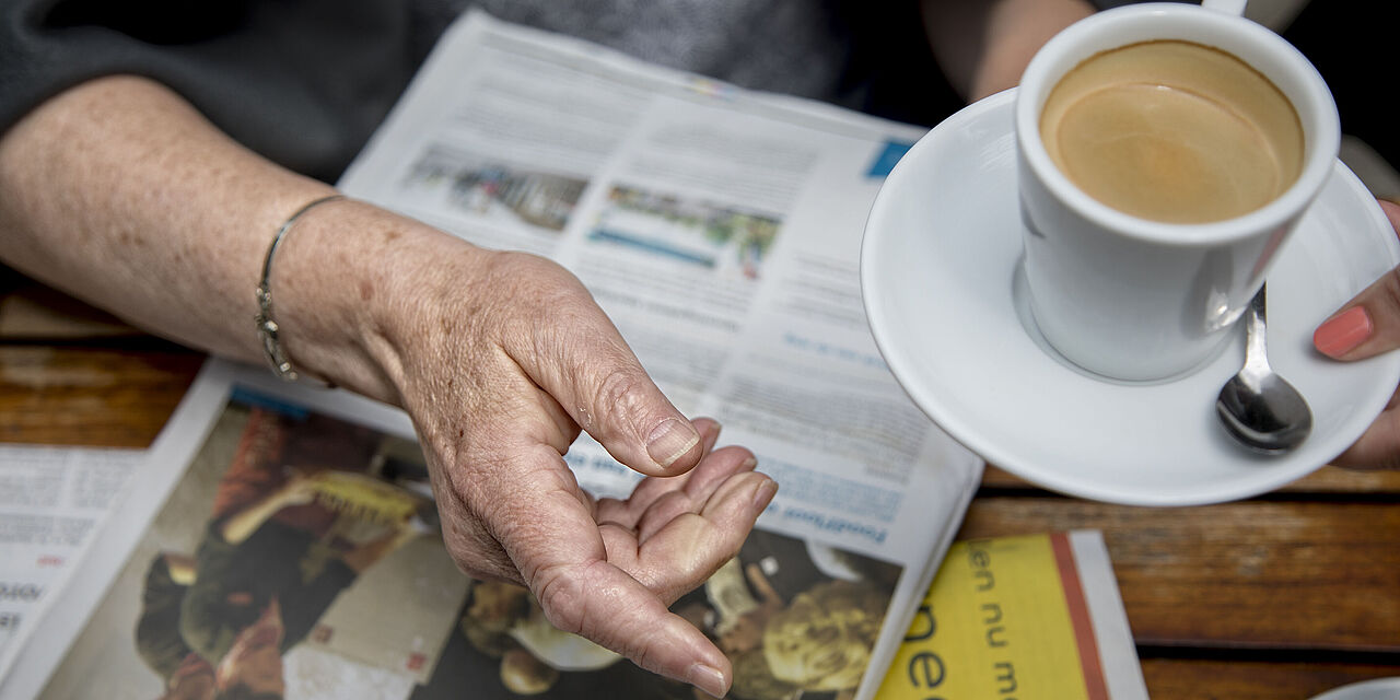 Hand van oudere dame met een kopje koffie en EdeStad krant op tafel