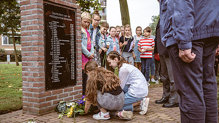 Twee meisjes leggen bloemen bij het Parkwegmonument in Ede